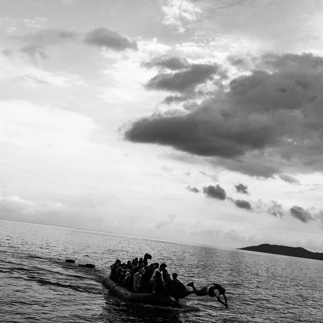 Hundreds of refugees landing in Lesbos, Greece. A young man dives from the boat towards the shore.