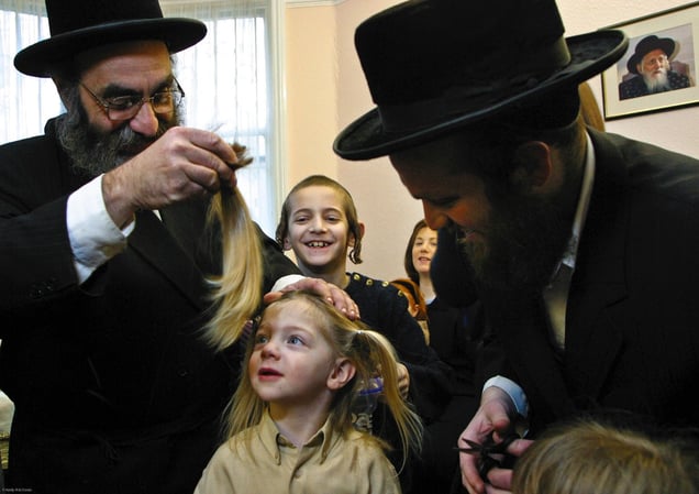 In Stamford Hill, London, United Kingdom on the 3rd birthday of a Orthodox Jewish boy he has his first ever hair cut leaving his peyos (sideburns) to grow. Here his Grandfather cuts the main part of his hair away watched closely by the boy, his father and family. He will now begin to learn the Torah.