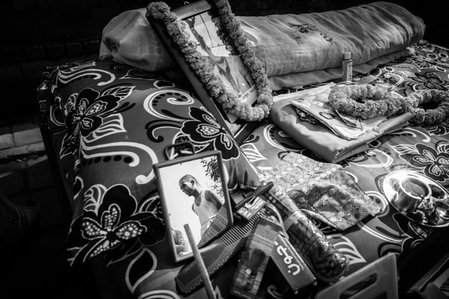 Navaraj seen in the reflection among the items provided as offering (daan) to the priest. The demanding rituals take a toll on their physical health; weaknesses, gastritis, and low blood pressures are common health problems among the professional mourners. Most of them, including Navaraj have strictly refrained their family members from visiting the Kriyaputri house when they are in.