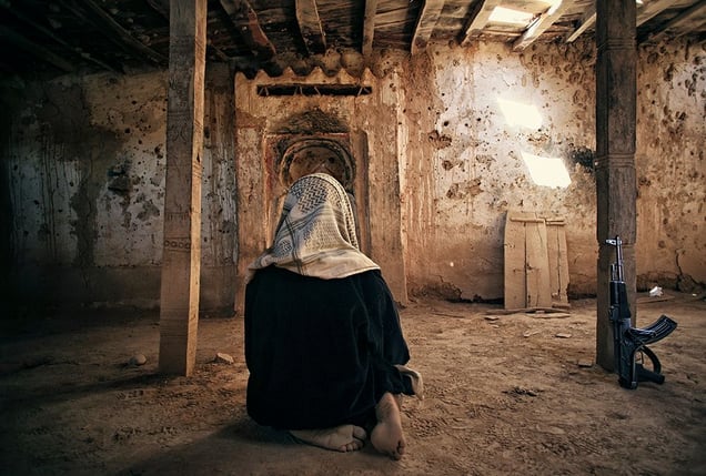 Shibam, Yemen: The boy that has leaned his rifle against the wall is praying in an old abandoned mosque in the desert, near the historical town in the Hadhramaut valley. © Matjaz Krivic