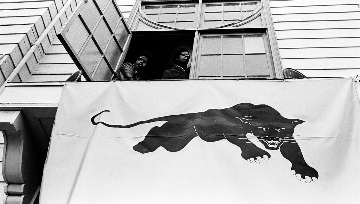 August 28, 1971 - Oakland, California, USA: During George Jackson’s funeral two Panthers look out at the enormous crowd gathered in the parking lot of a Safeway across the street from Augustine’s Church. Left is Clark Bailey, known as Santa Rita, a member of The Lumpen, the Panther singing group.