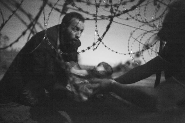 A man passes a baby through the fence at the Serbia/Hungary border in Röszke, Hungary, 28 August 2015.