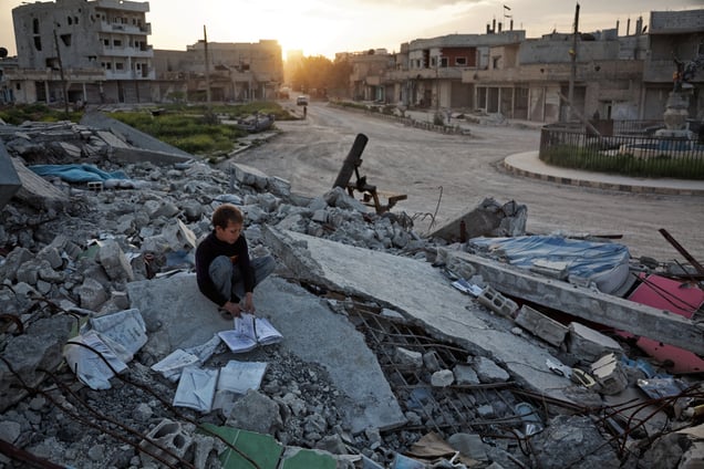 A Kurdish boy going through some books left in a destroyed building in Azadi square in Kobane on 20 April, 2015