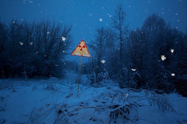 Near Pripyat, Ukraine, 2011. A radiation sign along the road warns of the danger. The tranquility of the sight on an evening of heavy snowfall belies the lingering threat in the peaceful winter landscape.