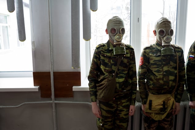 Students stand ready as a teacher observes how quickly they can dress in gask masks, 4 Apr 2016, School #7, Dmitrov, Russia. School #7 is a public school but offers cadet classes for those who wish to participate. The benefit of participating in cadet classes includes free lunch, while other students have to pay.