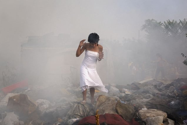 A girl runs through smoke near a suspected arson in an abandoned home in Nova Gazela, a camp on the New Belgrade side of the Sava River. The fire happened on the day before the relocation and destruction of the settlement. © Matt Lutton