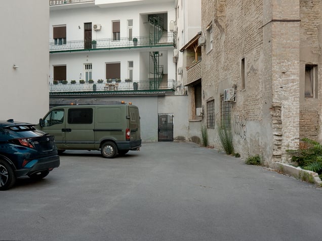 A courtyard in Novi Sad, Serbia. An older masonry structure and a newer residential block stand side by side, forming a compact record of overlapping urban layers.