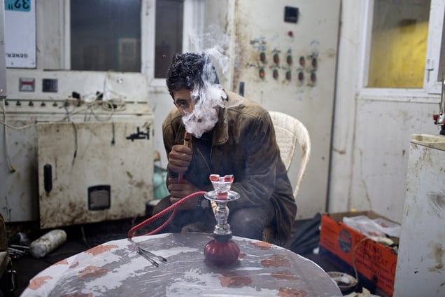 Jamal, 17, smokes flavored tobacco from a small hookah pipe inside the utility cabin. 19/02/15.