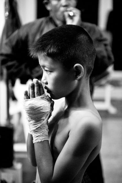 A boy is praying before the fight. His trainer smokes a cigarette at the background. © Sandra Hoyn