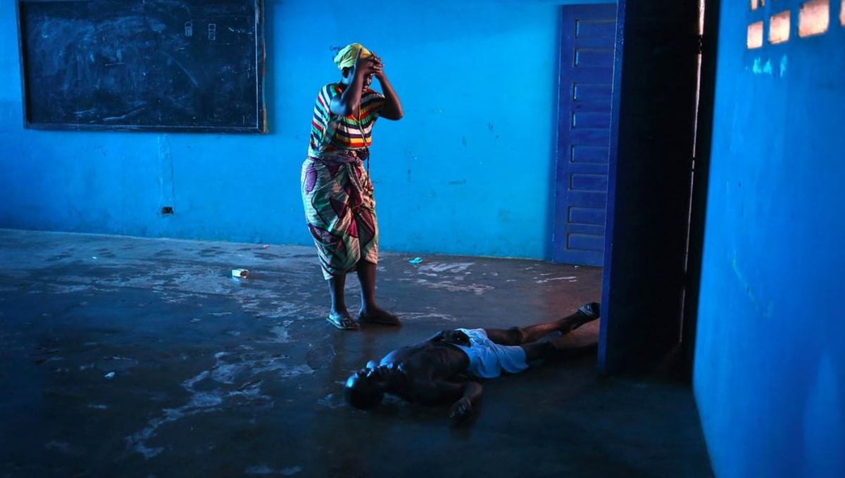 Blue Room. Omu Fahnbulleh stands over her husband Ibrahim after he fell and died in a classroom used for Ebola patients. From the series "Ebola Crisis Overwhelms Liberian Capital." Winner of L’Iris d’Or, 2015 Sony World Photography Awards.