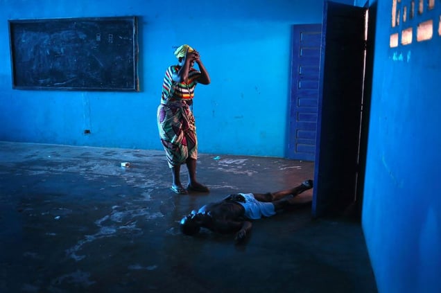 Blue Room. Omu Fahnbulleh stands over her husband Ibrahim after he fell and died in a classroom used for Ebola patients. From the series "Ebola Crisis Overwhelms Liberian Capital." Winner of L’Iris d’Or, 2015 Sony World Photography Awards.
