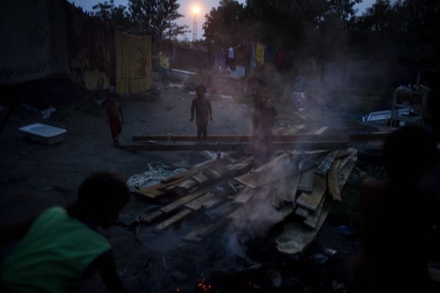 Children play near a garbage burn pile in the Stara Gazela camp at dusk. © Matt Lutton