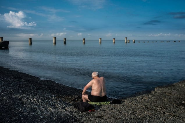Georgia, Ochamchira, AbkhaziaA man sits on a towel on a beach. In the background a construction project, which was destroyed in the war between Abkhazia and Georgia in 1992 - 1993, is visible.© Petrut Calinescu