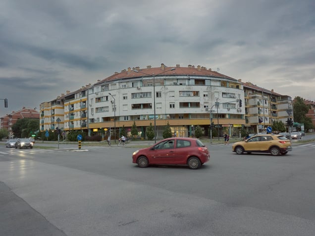 A residential-commercial block on Bulevar Slobodana Jovanovića in Novi Sad, Serbia. The curved façade and ground-floor businesses place the building within the later urban fabric of Novo Naselje.