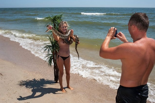 Ukraine, Zatoka A female tourist, holding a rented snake, poses for a photograph on a beach in front of a plastic palm tree in the cheap Black Sea resort destination of Zatoka.© Petrut Calinescu