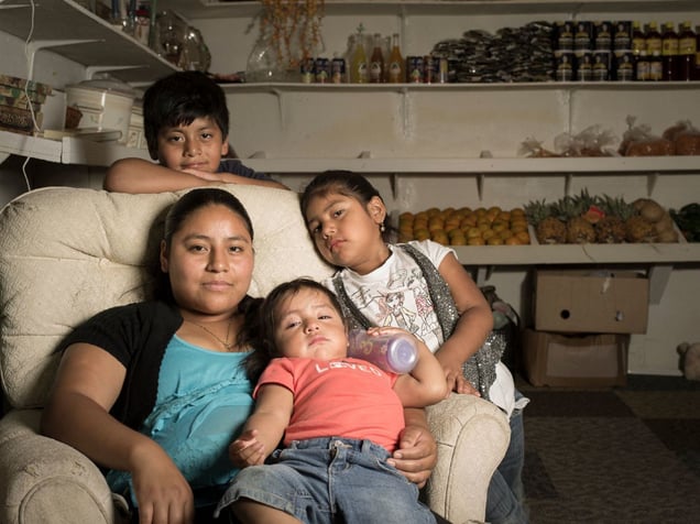 Herminia Hernandez-Bautista is shown with her three children in the fruit and vegetable stand she operates in the Franklin Flea and Craft Market in Franklin, NC. © Forest McMullin