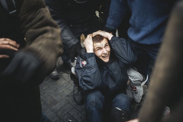 Police man covers the head from the blows of protesters, after being beaten by protesters during a clash between protesters and police. Kiev, Feb. 20, 2014