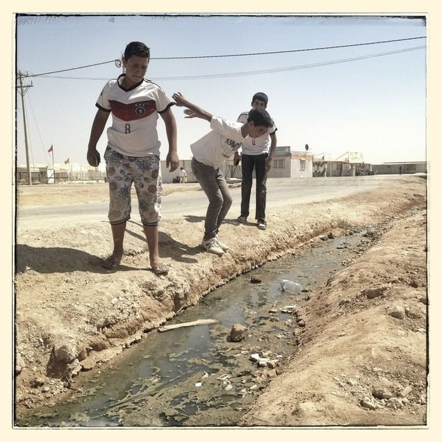 (left to right) Omar*, Salem* and Ali* prepare to jump over a waste water stream.
