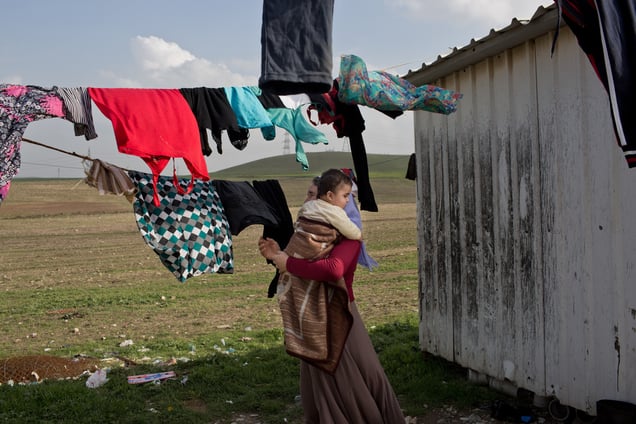 Ghazal hangs up the family laundry while holding her grandson, Mazal.The family of Yezidis, displaced from Sinjar, live next to an oil refinery in the Kurdish Region of Iraq. The young men run the refinery 24 hours a day with little to no safety equipment. 17/02/15, Tanjero, Iraq.