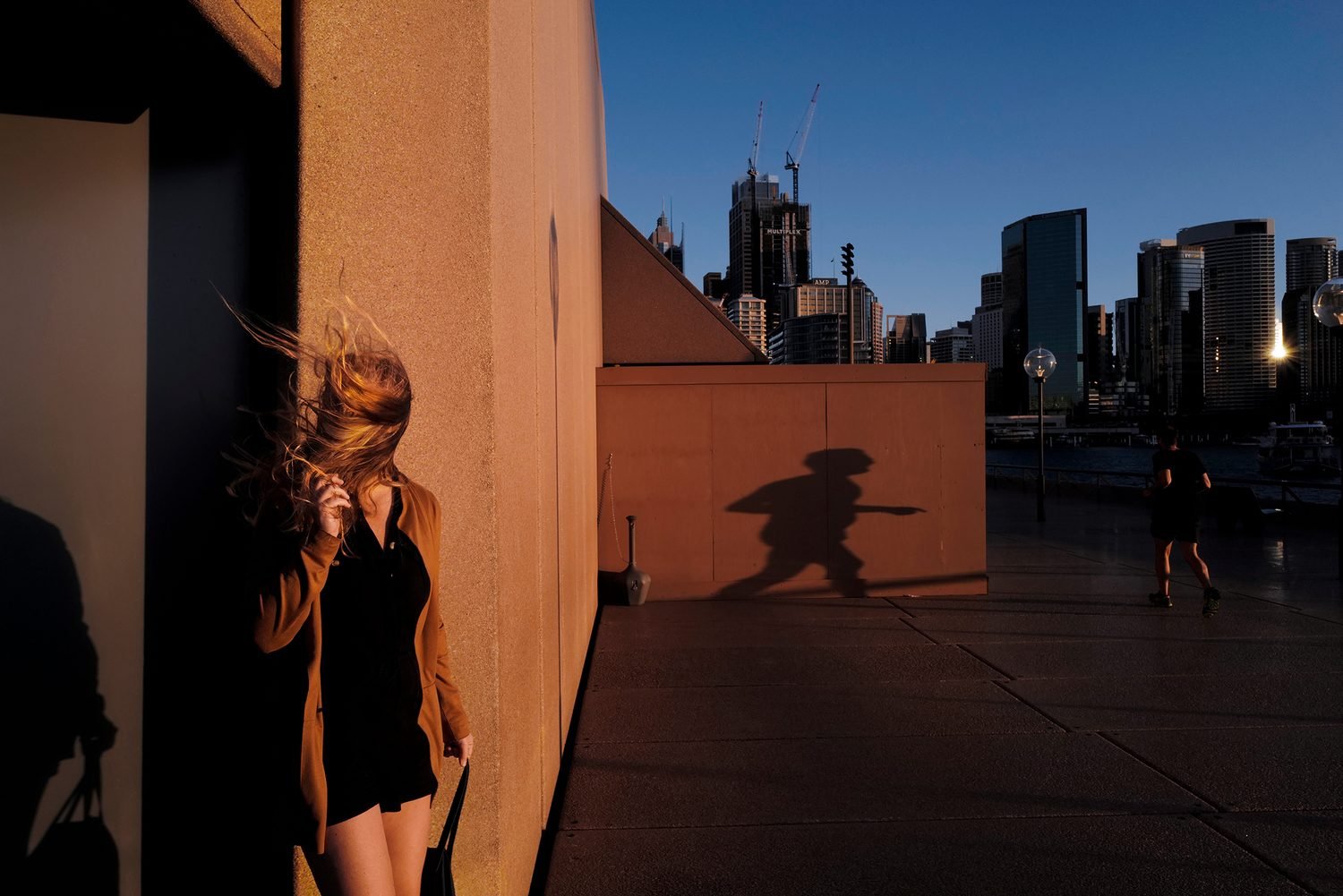 Windswept, 2020. The Winter wind whips through a near empty Sydney Opera House precinct, as joggers pass by and Sydney’s few remaining tourists grab a quick selfie in front of the iconic structures in the last minutes of golden, winter light. © Sam Ferris