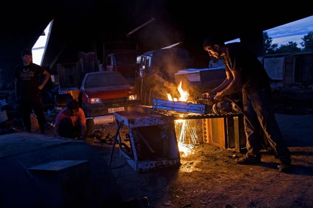 A man works at his metal salvage business in the Nova Gazela camp underneath the bridge. The enterprise employs dozens of people in the community. © Matt Lutton
