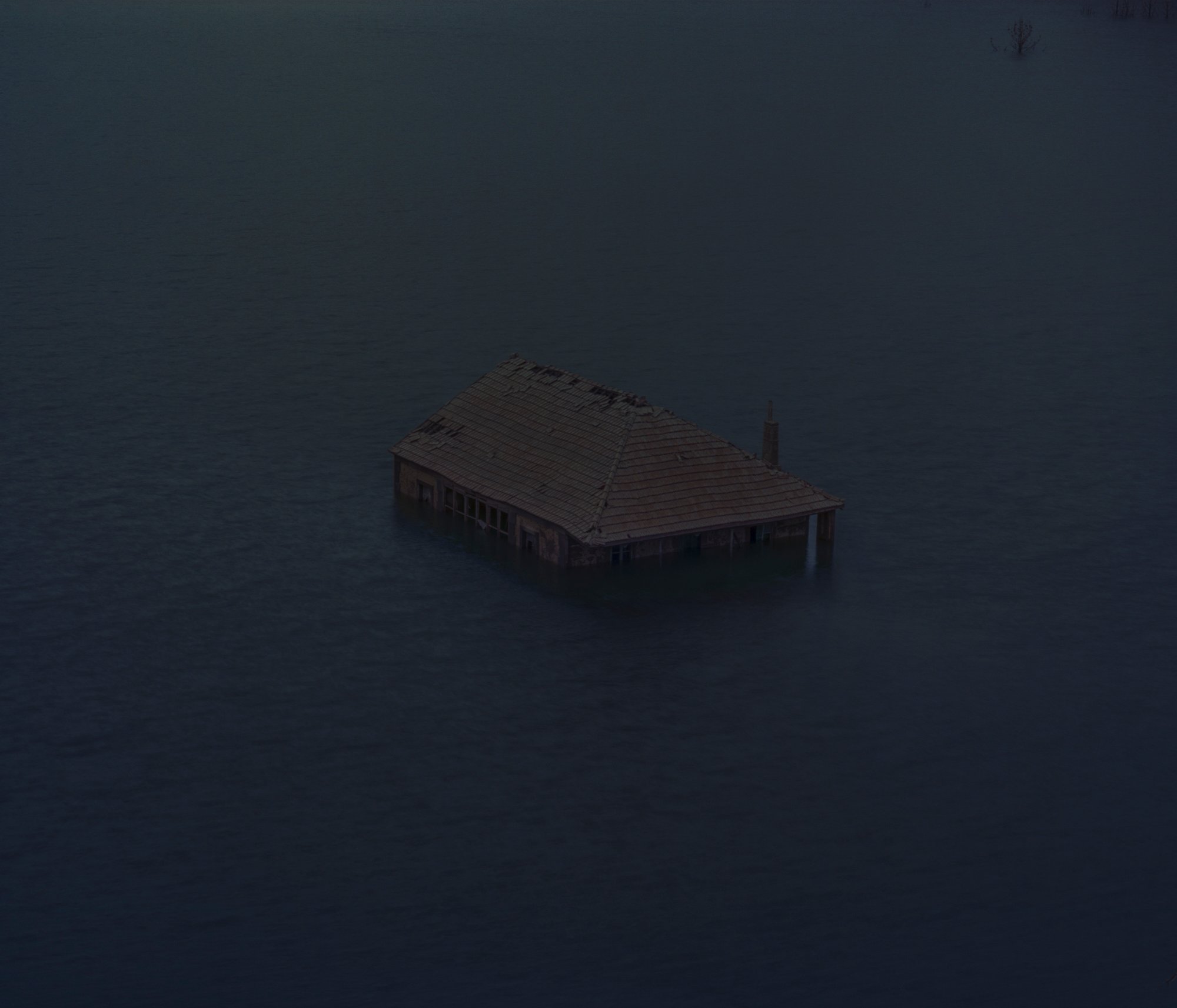 Ranger's home. In the 1970s, in the village of O Bao, located on the border between Galicia and Portugal, a house was built for the forest ranger to live in. His task was to safeguard the area’s forests, particularly to prevent wildfires. After the construction of the Limia River dam in the 1990s, the village of O Bao was completely submerged, including the forest ranger’s house, which resurfaced 30 years later due to the drought that had nearly emptied the reservoir. The house, seemingly floating on the water, appears like a ghost of the life that once thrived there. According to Francisco Gallato, a former resident of O Bao: “Perhaps the passage of time will one day heal all the pain caused by the abandonments brought about by the emigrations of the past.” © Carlos Folgoso Sueiro