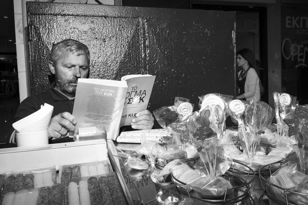 A lollipop seller reads Naomi Klein’s “Shock Doctrine” in Greek on Ermou Street, Athens (May 21, 2014)