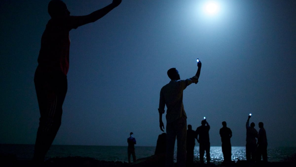 World Press Photo of the Year 2013.  African migrants on the shore of Djibouti city at night, raising their phones in an attempt to capture an inexpensive signal from neighboring Somalia—a tenuous link to relatives abroad. Djibouti is a common stop-off point for migrants in transit seeking a better life in Europe and the Middle East © John Stanmeyer, USA, VII for National Geographic