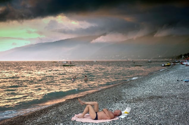 Gagra, Abkhazia. A man lies on a towel on the pebble beach at Gagra, the busiest seaside resort in Abkhazia. Dark clouds gather over the mountains in the distance. Gagra is a mere 20 kilometres from the Russian border.© Petrut Calinescu