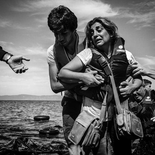 A woman is helped to the shore after a boat filled with refugees landed on the shore of Lesbos, Greece.