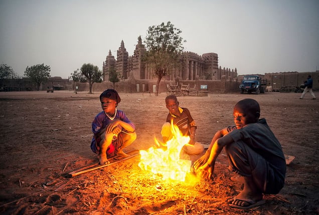 Djenné, Mali: A cold morning in front of the famous mud mosque where the children are warming up around the pile of burning rubbish. © Matjaz Krivic