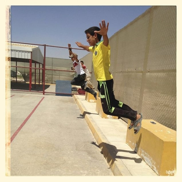 Children jump off concrete blocks in the sports pitch at Za'atari refugee camp