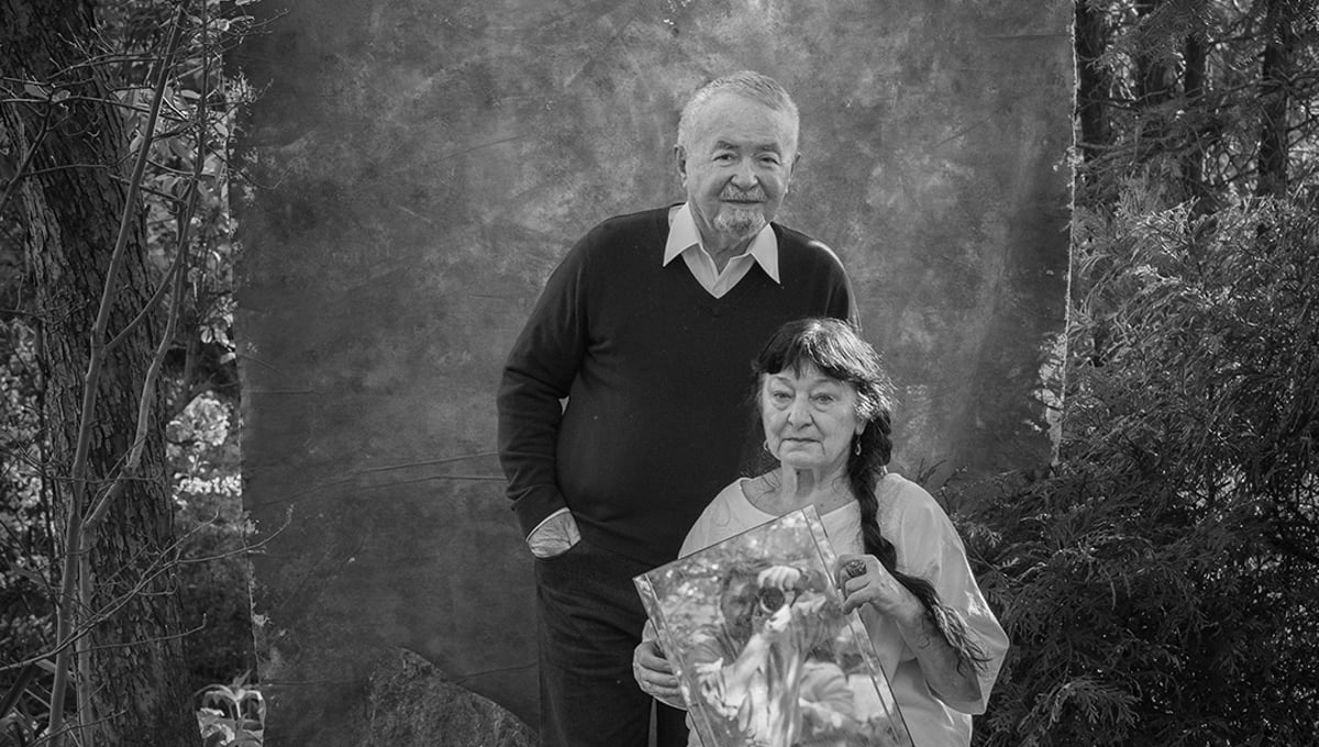 My parents in their garden while I appear as a reflection, held in my mother's hand. 

Reflected Presence.  Family photo.