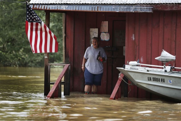 "A person is seen on the front porch of a home as it is surrounded by flood waters in Port Vincent, Louisiana". From the Series "Louisiana Flooding".