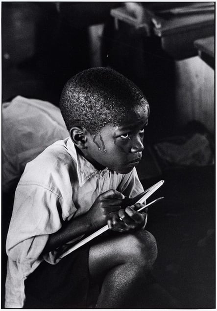 Bantu Education. An earnest boy squats on haunches and strains to follow the lesson in the heat of a packed classroom.