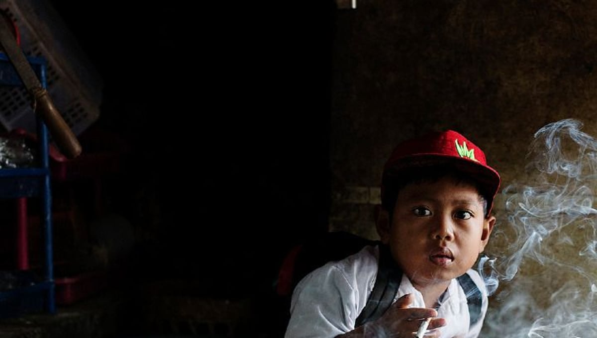 Dihan Muhamad, who used to smoke up to two packs of cigarettes a day before cutting down, has his first cigarette at 7AM at his home before he attends his first grade class in his village near the town of Garut in West Java, Indonesia. © Michelle Siu