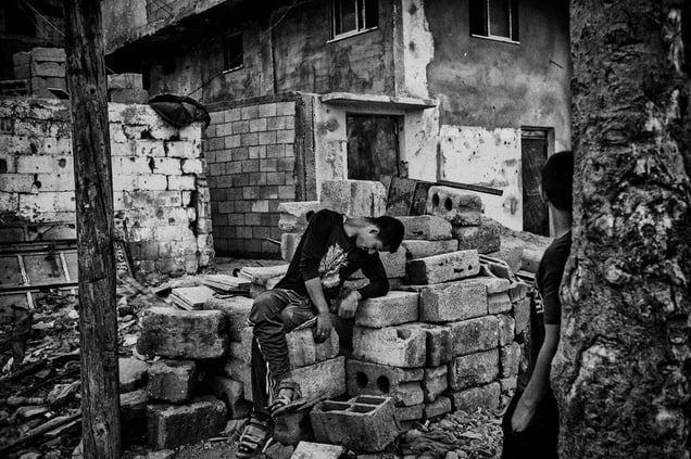 A young man rests near his destroyed house in the evening after a day of work
