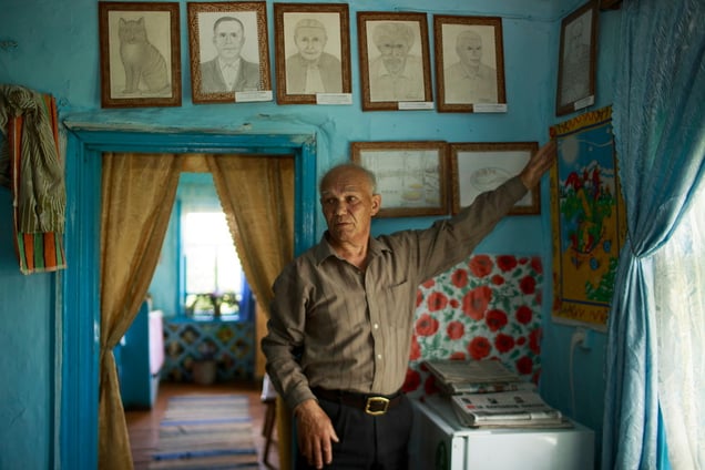 Alexey in his house in Bergul village, showcasing a gallery of portraits created by himself.