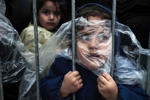 A child is covered with a raincoat while she waits in line to register at a refugee camp in Preševo, Serbia, 07 October 2015