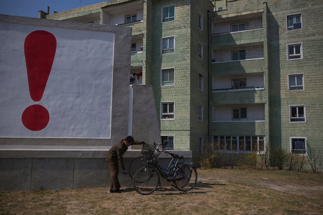 A man checks his bicycle next to a painted exclamation point on a propaganda billboard in Kaesong, North Korea, 24 April 2013.