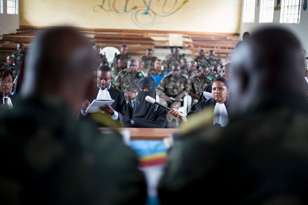 A victim testifies before the closed military tribunal.  A member of the prosecution team holds a microphone up for her while a defense lawyer makes notes. The accused soldiers are seated in the rear.  Victims are often extremely reluctant to step forward due to the stigma congolese society places on victims of rape. Even in Minova, only 47 victims testified.  © Diana Zeyneb Alhindawi