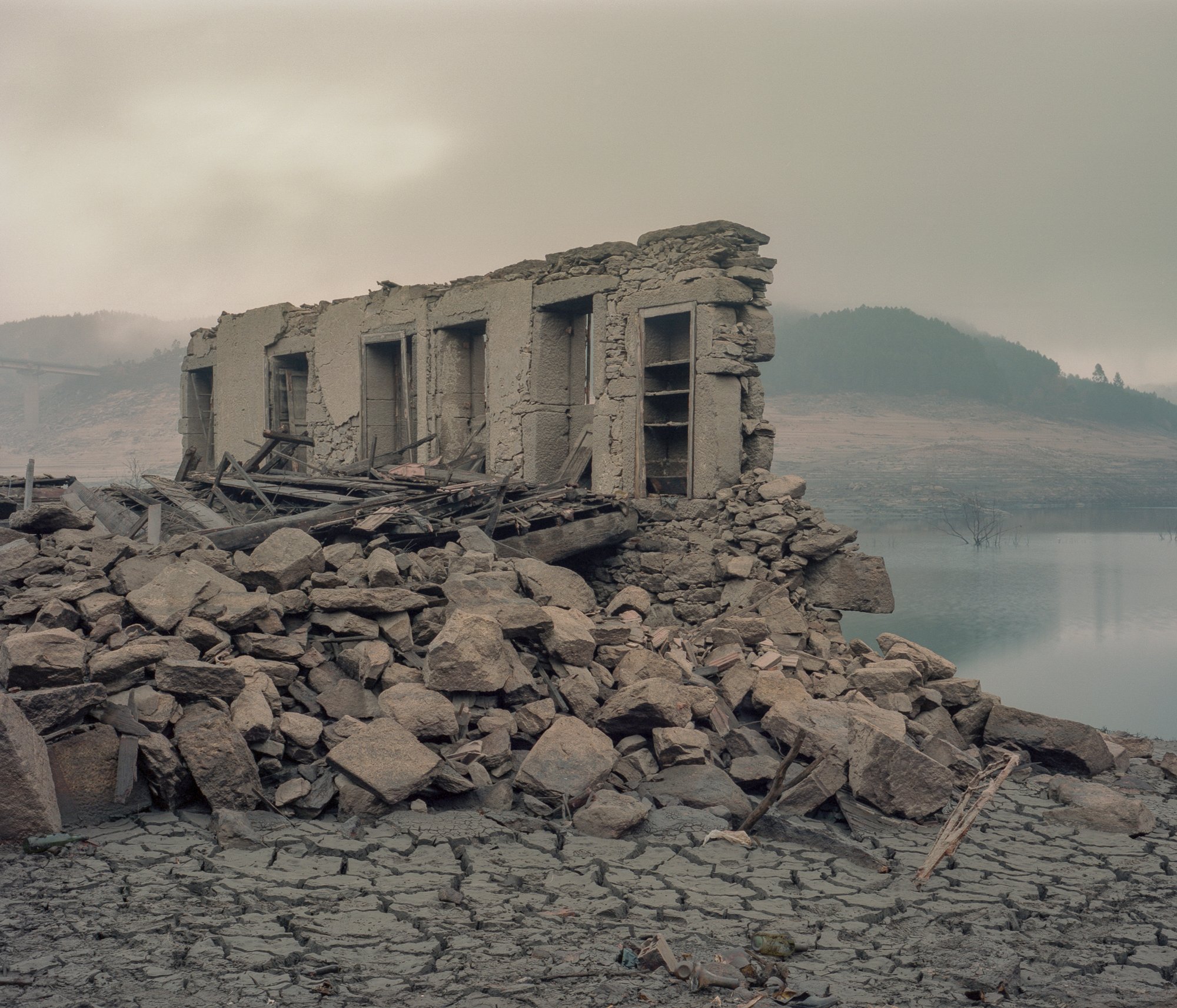 Aceredo. In January 1992, the Lindoso reservoir, managed by the Portuguese hydroelectric company EDP, submerged the towns of Aceredo, Buscacalque, O Bao, Lantemil, and A Reloeira, on the border between Galicia and Portugal. That fateful day froze those towns in time, marking the end of an era for its inhabitants. Three decades later, a severe drought has nearly drained the Lindoso Reservoir, exposing the remains of lives that once thrived there. In the picture, the remnants of a demolished house in one of these villages serve as a haunting reminder of the neglect that has befallen the entire region. © Carlos Folgoso Sueiro