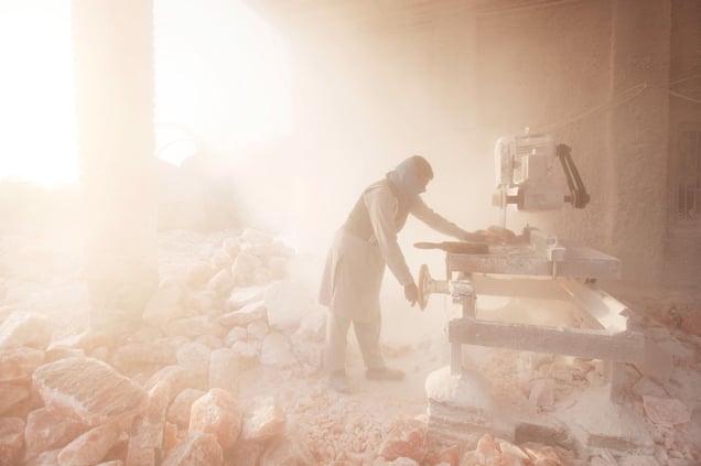 A salt carver cuts blocks of pink rock salt in to squares covering everything in fine salt dust outside the Khewra Salt mine.