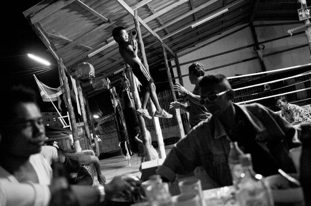 A boy is making exercise. In the front the trainer is drinking whiskey with his friends and the father. © Sandra Hoyn