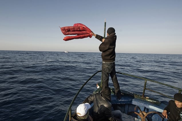 Strait of Sicily, Mediterranean Sea, April 2, 2011. A boat with more than 100 migrants from Tunisia waving at an Egyptian fishing boat to ask for directions to the Italian coast. © Giulio Piscitelli / Contrasto / Réa