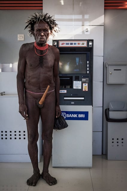 Asike Halu, 67, near the ATM machine of the BRI bank in Wamena town. Asike makes money from tourists, allowing them taking photos of him charging 5 to 10 thousand rupiahs (0.5 - 1 USD) per click and also providing them local guide services. Asike makes from 10 to 60 US dollars a day and keeps his money in the bank.Wamena, West Papua Province.