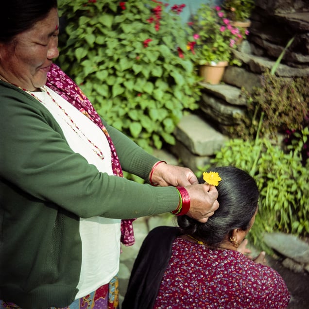 Sukmaya braids a flower into Baisamaya’s hair as they bask in the sun. Sukmaya is the more talkative one, while Baisamaya is more reserved. They do not call each other by name, using mitini instead.