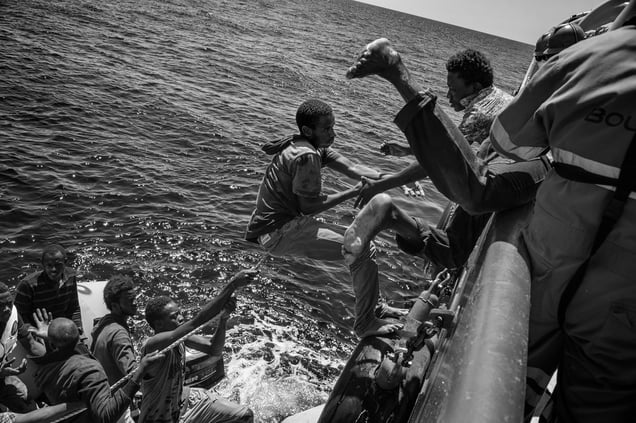 Migrants climb on board of a rescue ship by Doctors without Borders to escapetheir sinking rubber dinghy. Strait of Sicily, Mediterranean Sea, 21 August 2015.