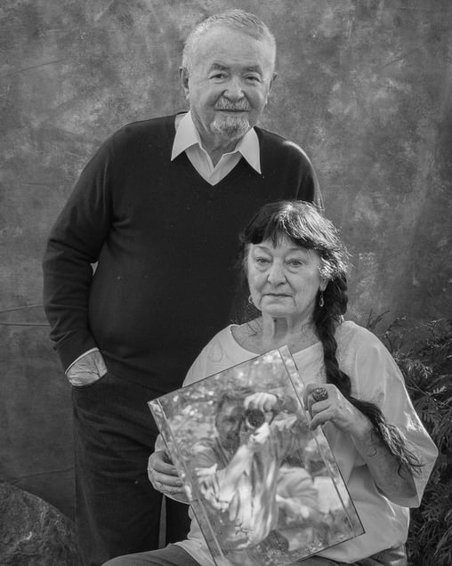 My parents in their garden while I appear as a reflection, held in my mother's hand. 

Reflected Presence.  Family photo.